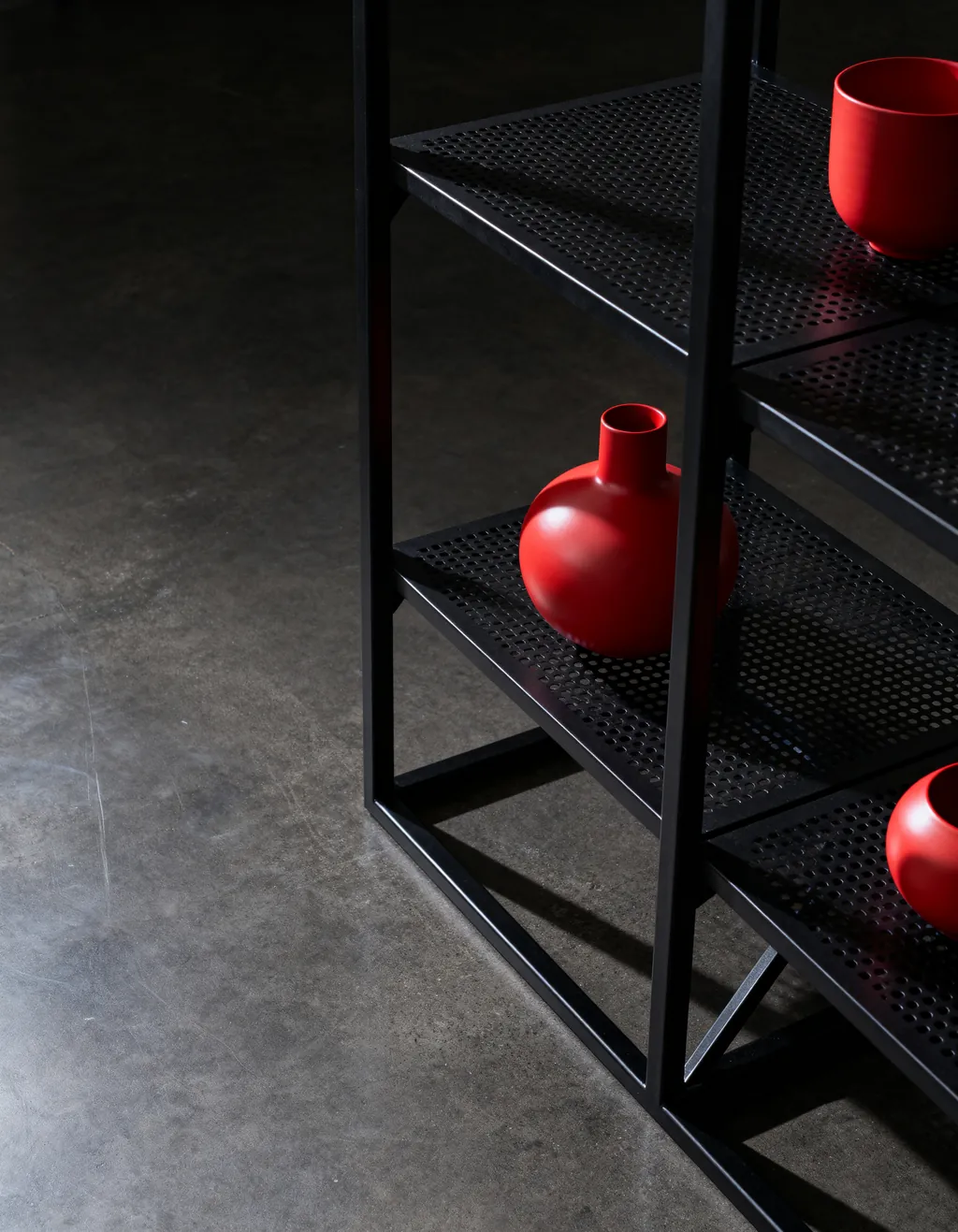 Concept image: open shelving of black steel floor grating holding red ceramic vessels
